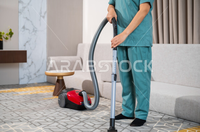 عاملة نظافة ترتدي اليونيفورم الخاص بالعمل تقوم بتنظيف البيت بالمكنسة الكهربائية، استقدام العمالة الاجنبية المنزليه المدربة، المهام والأعمال المنزلية الروتينية، جودة الخدمات في السعودية، مهن ووظائف نسائية