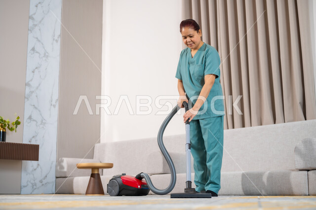 عاملة نظافة ترتدي اليونيفورم الخاص بالعمل تقوم بتنظيف البيت بالمكنسة الكهربائية، استقدام العمالة الاجنبية المنزليه المدربة، المهام والأعمال المنزلية الروتينية، جودة الخدمات في السعودية، مهن ووظائف نسائية