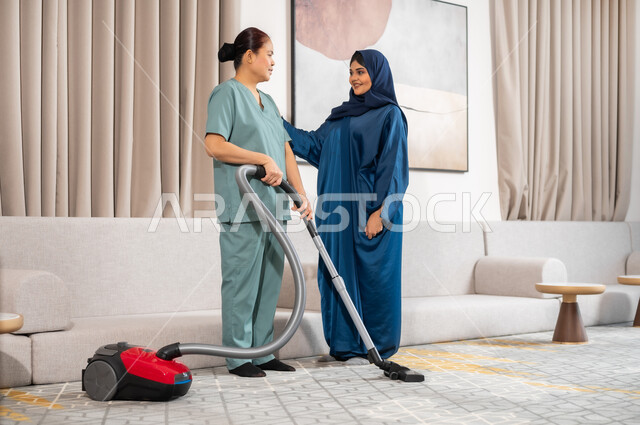ايماءات السعادة والرضا عن جودة خدمة العاملة، توفير خدمات العناية بالمنزل والنظافة والترتيب، سيدة عربية خليجية سعودية تعطي الارشادات والتوجيهات لخادمة فلبينية تقوم باستخدام المكنسة الكهربائية، استقدام العمالة الخارجية المرخصة والمؤهلة