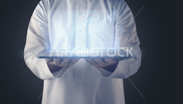صورة مقربة لرجل عربي سعودي خليجي يحمل بيديه جهاز تقني ذكي عليه رسومات بيانية ثلاثية الأبعاد بتقنية الهولوجرام ،  صعود و نزول البورصة المالية ، الاستثمار المالي و الاقتصادي ، تطور و ابتكار .