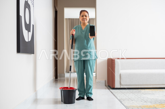 الاهتمام بالتنظيف والقيام بالمهام الروتينة، عاملة نظافة تنظر الى الكاميرا ترتدي اليونيفورم الخاص بالعمل وتقوم بمسح وتنظيف البيت، عرض شاشة سوداء فارغة على الهاتف المحمول، استقدام العمالة الاجنبية المنزليه المدربة، جودة الخدمات في السعودية، مهن ووظائف نسائية