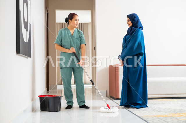 توفير خدمات العناية بالمنزل والنظافة والترتيب، ايماءات السعادة والرضا عن جودة خدمة العاملة، سيدة عربية خليجية سعودية تعطي الارشادات والتوجيهات لخادمة فلبينية تقوم بمسح وتطهير المكان، استقدام العمالة الخارجية المرخصة والمؤهلة