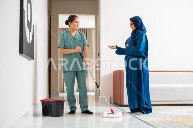 استقدام العمالة الخارجية المرخصة والمؤهلة، توفير خدمات العناية بالمنزل والنظافة والترتيب،  سيدة عربية خليجية سعودية تعطي الارشادات والتوجيهات لخادمة فلبينية تقوم بمسح وتطهير المكان، ايماءات السعادة والرضا عن جودة خدمة العاملة