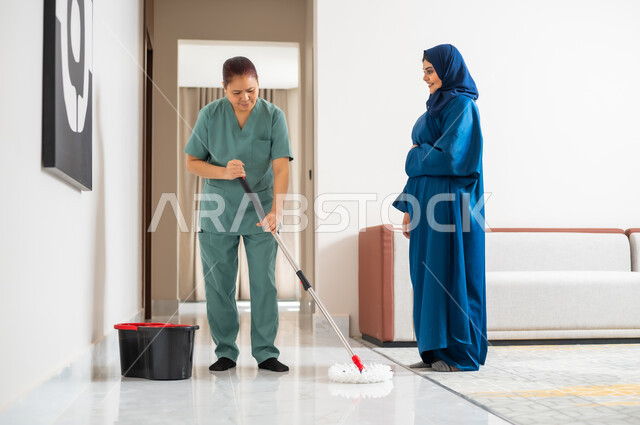توفير خدمات العناية بالمنزل والنظافة والترتيب، ايماءات السعادة والرضا عن جودة خدمة العاملة، سيدة عربية خليجية سعودية تعطي الارشادات والتوجيهات لخادمة فلبينية تقوم بمسح وتطهير المكان، استقدام العمالة الخارجية المرخصة والمؤهلة