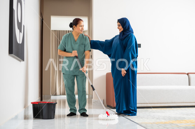 ايماءات السعادة والرضا عن جودة خدمة العاملة، توفير خدمات العناية بالمنزل والنظافة والترتيب، سيدة عربية خليجية سعودية تعطي الارشادات والتوجيهات لخادمة فلبينية تقوم بمسح وتطهير المكان، استقدام العمالة الخارجية المرخصة والمؤهلة