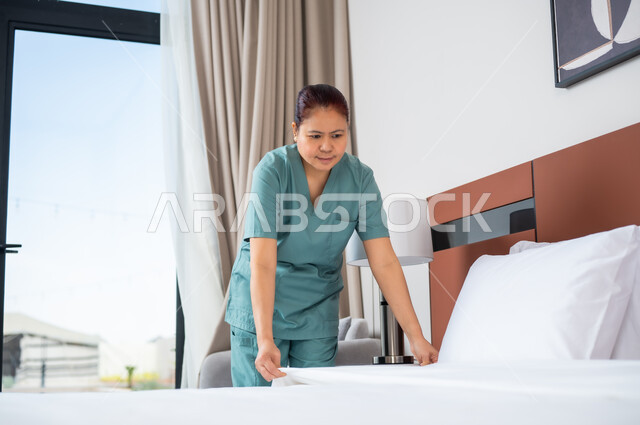 القيام بالمهام والأعمال الروتينية، عاملة فلبينية ترتدي اليونيفورم الخاص بالعمل تقوم بترتيب السرير في غرفة النوم، استقدام العمالة الاجنبية المدربة والمؤهلة من الخارج، مهن ووظائف نسائية, توفيرخدمات العناية وترتيب المنزل، الخادمات في البيوت السعودية