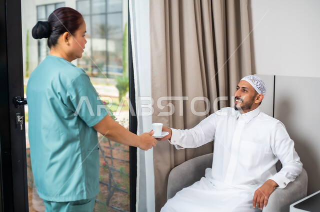 الخادمات في البيوت السعودية، القيام بالمهام والأعمال المنزلية الروتينية، المعاملة الحسنة للخادمة الاجنبية، مهن ووظائف نسائية, سيد عربي خليجي سعودي مع عاملة فلبينية ترتدي اليونيفورم الخاص بالعمل تقوم بتقديم القهوة، حسن الضيافة والاستقبال