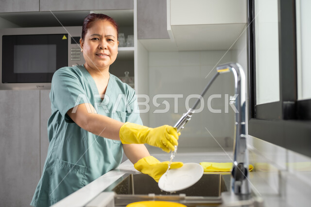 القيام الأعمال المنزلية الروتينية، أداء مهام المطبخ, عاملة أجنبية ترتدي اليونيفورم الخاص والقفازات تقوم بغسيل الأطباق باستخدام اسفنجة الجلي, استقطاب العمالة الأجنبية المرخصة والمؤهلة من الخارج, التطهير والتنظيف وغسل المواعين