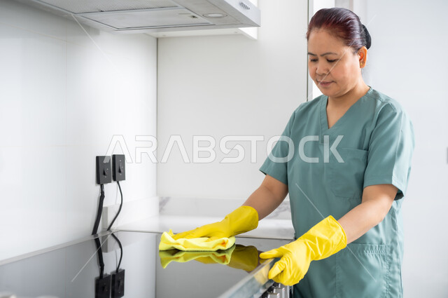 Attracting licensed and qualified foreign workers from abroad, disinfection and cleaning in homes, performing kitchen tasks, a foreign worker wearing a special uniform and gloves cleaning the gas, maids in the homes of the Kingdom of Saudi Arabia.