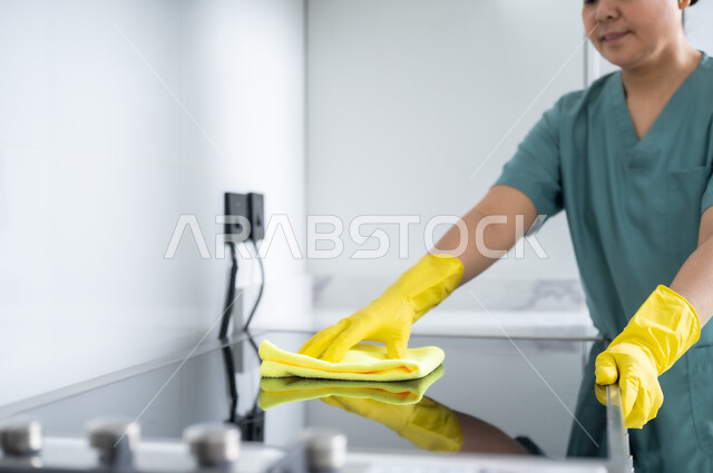 أداء مهام المطبخ، استقطاب العمالة الأجنبية المرخصة والمؤهلة من الخارج، عاملة أجنبية ترتدي اليونيفورم الخاص والقفازات تقوم بمسح الغاز، الخادمات في بيوت المملكة العربية السعودية، التطهير والتنظيف في المنازل