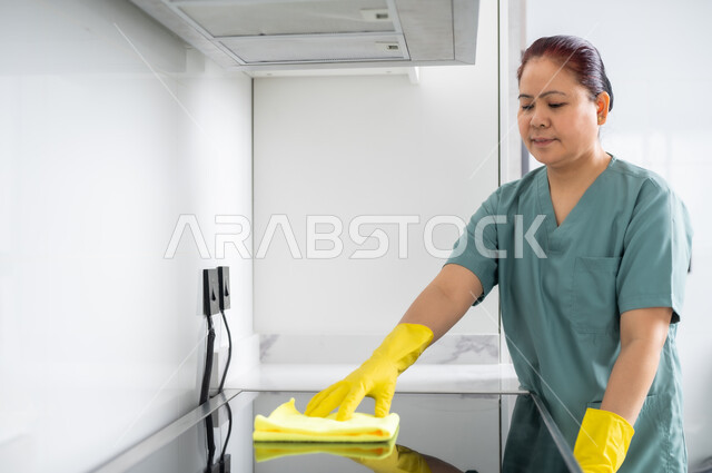 استقطاب العمالة الأجنبية المرخصة والمؤهلة من الخارج، التطهير والتنظيف في المنازل, أداء مهام المطبخ، عاملة أجنبية ترتدي اليونيفورم الخاص والقفازات تقوم بمسح الغاز، الخادمات في بيوت المملكة العربية السعودية