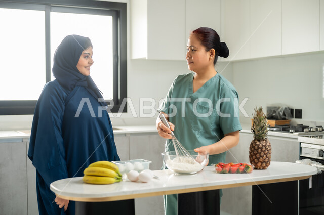 اعداد الحلويات الشهية في المطبخ, عاملة أجنبية ترتدي اليونيفورم الخاص تقوم بصنع الحلى برفقة ربة المنزل, تحضير وتجهيز المكونات اللازمة, تشغيل العاملات المرخصة والمؤهلة من الشركات والمكاتب السعوديه