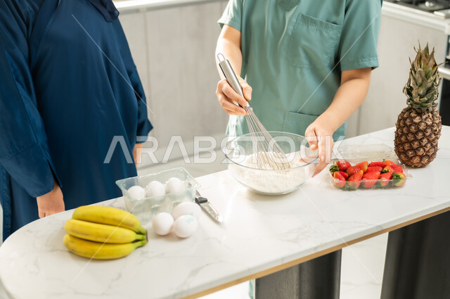 تحضير وتجهيز المكونات اللازمة, اعداد الحلويات الشهية في المطبخ, عاملة أجنبية ترتدي اليونيفورم الخاص تقوم بصنع الحلى برفقة ربة المنزل, تشغيل العاملات المرخصة والمؤهلة من الشركات والمكاتب السعوديه