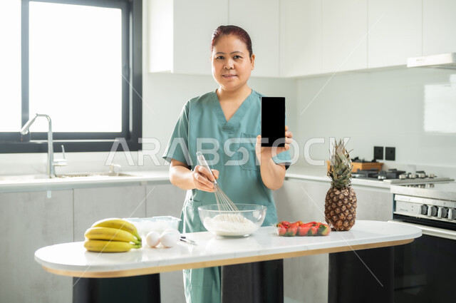 Displaying a blank black screen on the mobile phone, preparing delicious sweets in the kitchen, a worker wearing a special uniform mixing the ingredients and amounts, employing licensed and qualified workers from Saudi companies and offices, hiring a foreign maid for domestic services, preparing and processing the desserts.