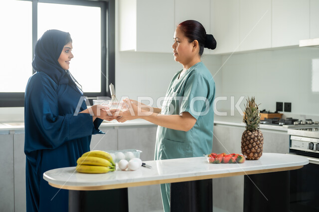 تحضير وتجهيز المكونات اللازمة, اعداد الحلويات الشهية في المطبخ, عاملة أجنبية ترتدي اليونيفورم الخاص تقوم بصنع الحلى برفقة ربة المنزل, تشغيل العاملات المرخصة والمؤهلة من الشركات والمكاتب السعوديه