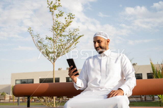 استخدام الأجهزة والتقنيات الحديثة والمتطورة, اجراء مكالمة فيديو عبر الهاتف المحمول, الجلسات والأجواء الهادئة في النهار, رجل عربي خليجي سعودي يرتدي الثوب التقليدي يقوم باستخدام الجوال, التسلية والترفيه عبر السوشال ميديا