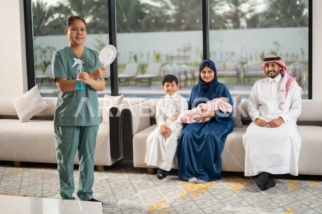 التنظيف والاهتمام بالأعمال الروتينية اليومية,  توفير خدمات العناية بالمنزل والنظافة والترتيب، عاملة أجنبية ترتدي اليونيفورم الخاص تحمل ادوات التنظيف تنظر الى الكاميرا عائلة بايماءات السرور، استقطاب عاملات أجنبيات مرخصة ومؤهلة من الخارج