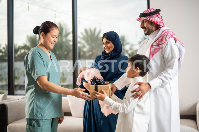 Kindness in dealing with domestic maids in Saudi Arabia, bringing in licensed and qualified foreign workers, a happy family atmosphere full of appreciation and respect, a Saudi-Gulf Arab child offering a gift box to a Filipina maid for the quality of her service and performance, women’s professions and jobs.