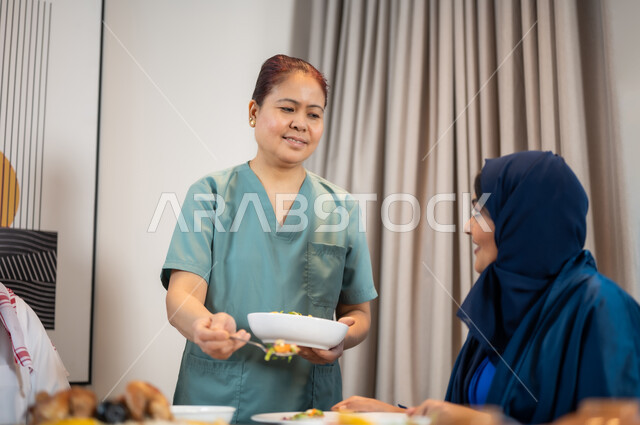 عاملة أجنبية تقوم بتحضير المائدة, سفرة مليئة بالمأكولات العربية الشرقية, وجبات وأطباق وأصناف متنوعة شهية,  استقطاب العاملات الأجنبيات من الخارج، جلسات وأجواء سعيدة, عائلة عربية خليجية سعودية تستمتع بتناول الطعام