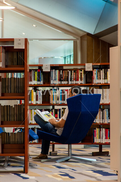 اكتساب المعرفة وتنمية الذخيرة اللغوية، قارئ عربي خليجي اماراتي يجلس على كنبة ويقوم بقراءة كتاب في مكتبة محمد بن راشد في امارة دبي، التصاميم الداخلية والديكورات للمكتبات العلمية في الامارات العربية المتحدة، مكان للقراء ومحبي العلم والمعرفة، تأمين وسائل الراحة للقراء