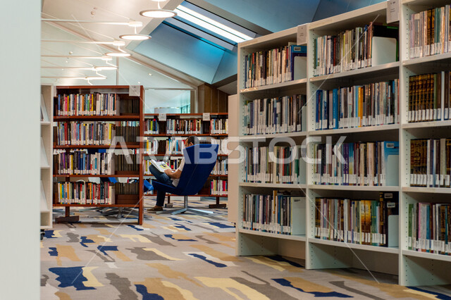 اكتساب المعرفة وتنمية الذخيرة اللغوية، قارئ عربي خليجي اماراتي يجلس على كنبة ويقوم بقراءة كتاب في مكتبة محمد بن راشد في امارة دبي، التصاميم الداخلية والديكورات للمكتبات العلمية في الامارات العربية المتحدة، مكان للقراء ومحبي العلم والمعرفة، تأمين وسائل الراحة للقراء