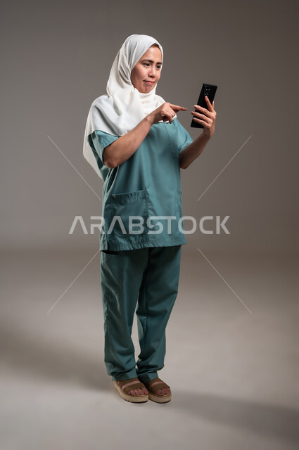 Chat with friends and relatives, keeping up with technical development and technological progress, using modern and advanced technical devices, portrait of a Filipina worker holding a mobile phone, full length of the body, gray background