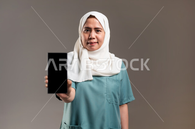 مواكبة التطور التقني والتقدم التكنولوجي، استخدام الأجهزة التقنية الحديثة والمتطورة، بورتريه لعاملة فلبينية تحمل هاتف محمول،خلفية رمادية