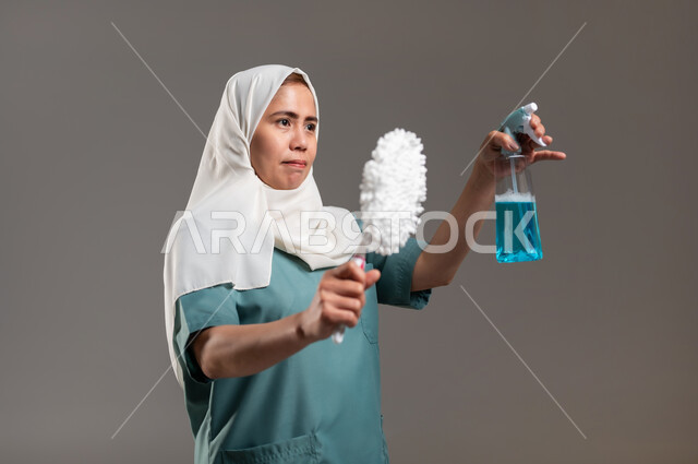 ممسحة وملمع اسطح، الاهتمام بنظافة وتطهير البيت والقيام بالمهام الروتينية, مهن ووظائف نسائية، بورتريه لعاملة منزلية فلبينية محجبة تحمل بيدها أدوات تنظيف المنزل، خلفية رمادية