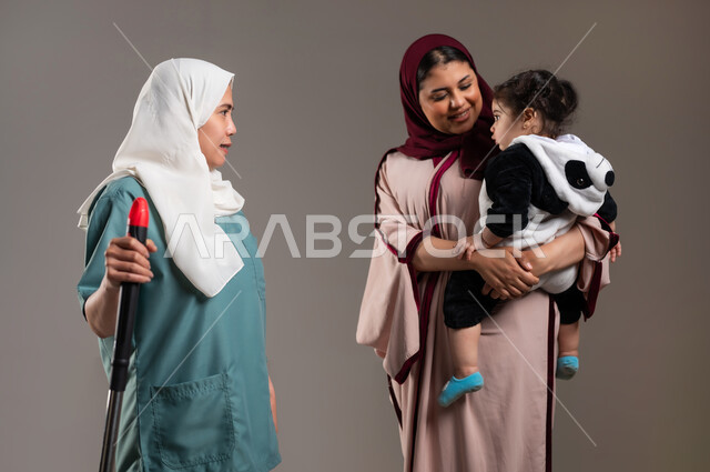 Expressions of love and affection between the child and the maid, portrait of a Saudi Arabian Gulf woman holding her child with gestures of joy, a Filipino worker holding house cleaning tools in her hands, preparing to do housework, bringing in workers from abroad, gray background