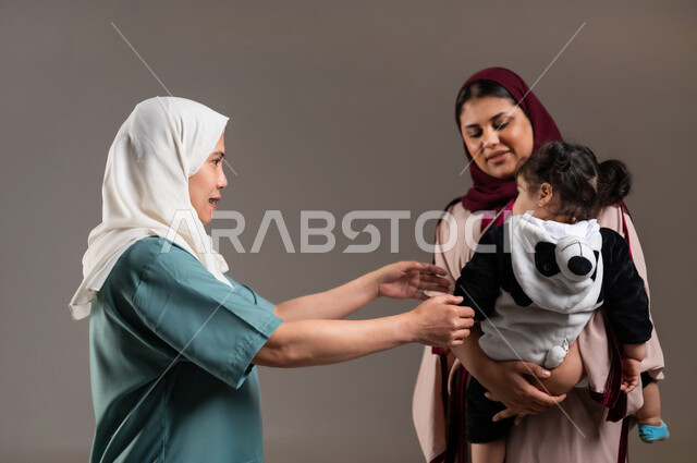 Modesty of women in dealing with maids in Saudi homes, portrait of a Filipino nanny taking the child from her mother with expressions of pleasure, concept of requesting care and attention for children, bringing in workers from abroad, gray background