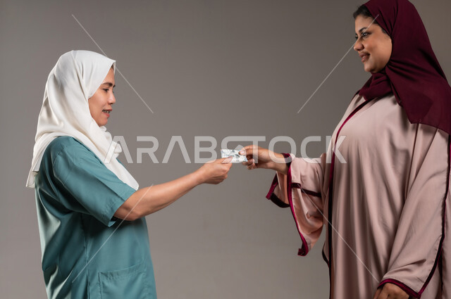 Kindness in dealing with maids in Saudi homes, portrait of a Saudi Gulf Arab woman wearing a colorful abaya handing the salary to the domestic worker with gestures of gratitude and pleasure, receiving the monthly pension, gray background