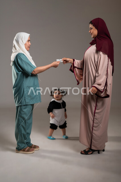 استلام المعاش الشهري، الإحسان في التعامل مع الخادمات في البيوت السعودية، بورتريه لامرأة ترتدي عباءة ملونة تقوم بتسليم الراتب للعاملة المنزلية بايماءات الشكر والسرور، الجسم بالطول الكامل، خلفية رمادية