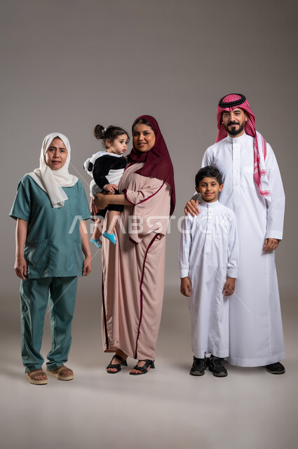 توثيق اللحظات بصورة عائلية جماعية، بورتريه لعائلة عربية خليجية سعودية وعاملة فلبينية يقومون بالتقاط الصور  , أجواء مليئة بالحب، الاهتمام بمشاعر الغير، قضاء أوقات ممتعه, الطول الكامل للجسم، خلفية رمادية