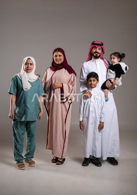 توثيق اللحظات بصورة عائلية جماعية، بورتريه لعائلة عربية خليجية سعودية وعاملة فلبينية يقومون بالتقاط الصور  , أجواء مليئة بالحب، الاهتمام بمشاعر الغير، قضاء أوقات ممتعه, الطول الكامل للجسم، خلفية رمادية