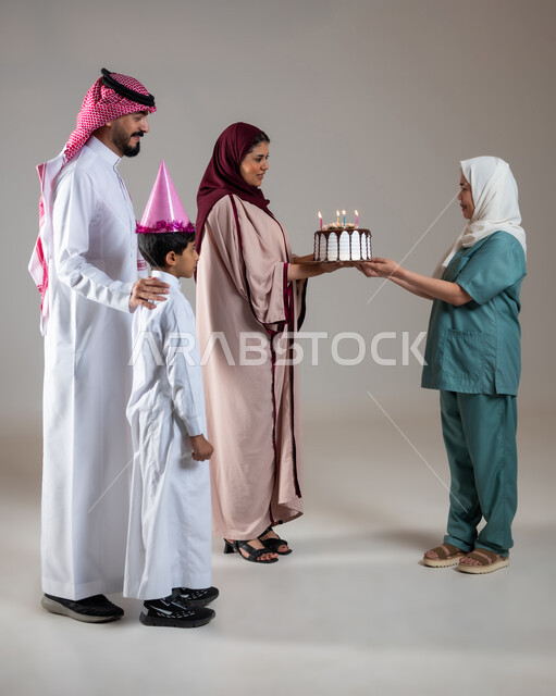 قضاء أوقات ممتعه بالمناسبات وأعياد الميلاد, بورتريه لعائلة عربية سعودية خليجية تحتفل بالعاملة الفيلبينية وتقدم لها قالب الكيك المزين بالشموع، ايماءات وجه تدل على السعادة و السرور, أجواء مليئة بالحب، الاهتمام بمشاعر الغير، الطول الكامل للجسم, خلفية رمادية
