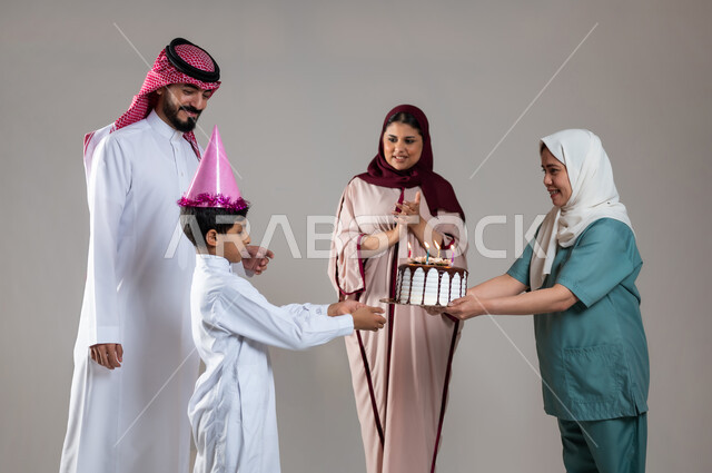 Facial gestures indicating happiness and pleasure, an atmosphere full of love, spending enjoyable times on occasions and birthdays, a portrait of a Saudi Arabian Gulf family celebrating the Filipina worker and offering her a cake decorated with candles, concern for the feelings of others, gray background