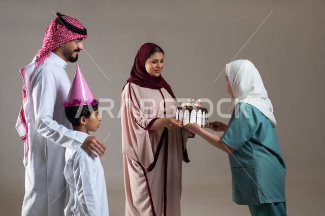 Facial gestures indicating happiness and joy, spending enjoyable times on occasions and birthdays, a portrait of a Saudi Arabian Gulf family celebrating the Filipina worker and offering her a cake decorated with candles, an atmosphere full of love, concern for the feelings of others, a gray background