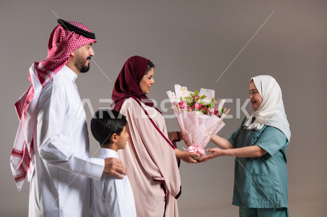 أعياد ومفاجآت ومناسبات سعيدة، أجواء مليئة بالتقدير والاحترام، بورتريه لعائلة عربية سعودية خليجية تقوم بتقديم باقة من الزهور لعاملة فلبينية بايماءات السعادة و السرور, الاهتمام بمشاعر الغير، خلفية رمادية