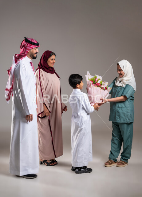 أجواء مليئة بالتقدير والاحترام، مشاركة وتقديم الهدايا بالمناسبات وأعياد الميلاد, بورتريه لعائلة عربية سعودية خليجية تقوم بتقديم باقة من الزهور لعاملة فلبينية بايماءات السعادة و السرور, الاهتمام بمشاعر الغير، الطول الكامل للجسم, خلفية رمادية
