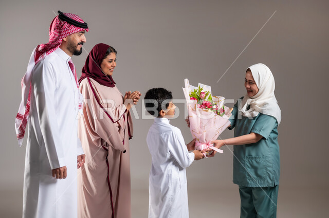 أعياد ومفاجآت ومناسبات سعيدة، أجواء مليئة بالتقدير والاحترام، بورتريه لعائلة عربية سعودية خليجية تقوم بتقديم باقة من الزهور لعاملة فلبينية بايماءات السعادة و السرور, الاهتمام بمشاعر الغير، خلفية رمادية