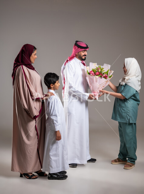 أجواء مليئة بالتقدير والاحترام، مشاركة وتقديم الهدايا بالمناسبات وأعياد الميلاد, بورتريه لعائلة عربية سعودية خليجية تقوم بتقديم باقة من الزهور لعاملة فلبينية بايماءات السعادة و السرور, الاهتمام بمشاعر الغير، الطول الكامل للجسم, خلفية رمادية
