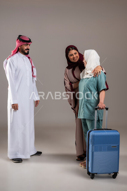 تأجيرالعمالة الخارجية المرخصة والمؤهلة من الخارج، بورتريه لرجل وامرأة عربيان سعوديان خليجيان يستقبلان عاملة فلبينية ترتدي اليونيفورم الخاص بالعمل وتمسك بيدها حقيبة السفر، المعاملة الحسنة للخادمات، الطول الكامل للجسم, خلفية رمادية