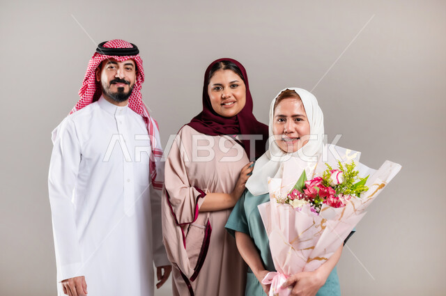 المعاملة الحسنة للخادمات، النظر الى الكاميرا بايماءات الشكر والامتنان لجودة خدمة واداء العاملة المنزلية، بورتريه لرجل وامرأة عربيان سعوديان خليجيان يقدمان باقة زهور الى العاملة  الفلبينية، استقدام العمالة الخارجية المرخصة والمؤهلة، مهن ووظائف نسائية، خلفية رمادية