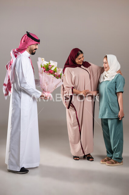الإحسان في التعامل مع الخادمات في البيوت السعودية، القيام بالمهام والأعمال المنزلية الروتينية، بورتريه لرجل وامرأة عربيان سعوديان خليجيان يقومان بتقديم باقة زهور للعاملة الفلبينية لجودة خدمتها وادائها، مهن ووظائف نسائية، الطول الكامل للجسم, خلفية رمادية