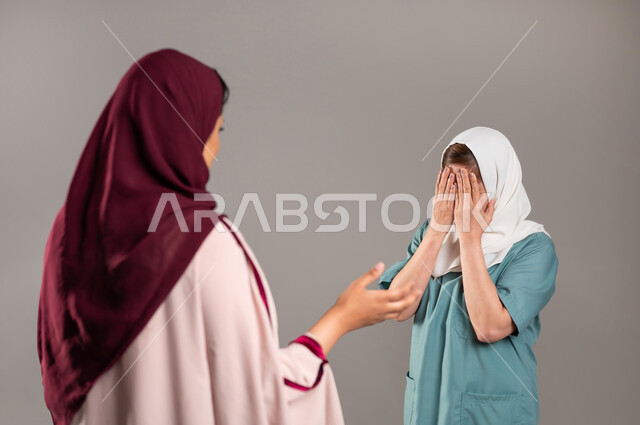 الغضب والقاء اللوم، بورتريه مقرب من الخلف لامرأة عربية خليجية سعودية محجبة ترتدي عباءة ملونة تقوم بإعطاء تنبيهات لعاملة منزلية بتعابير حادة، عدم انجاز العمل حسب المطلوب، التعصب والتوتر الانفعالي، خادمة فلبينية تبكي بايماءات الخوف، خلفية رمادية