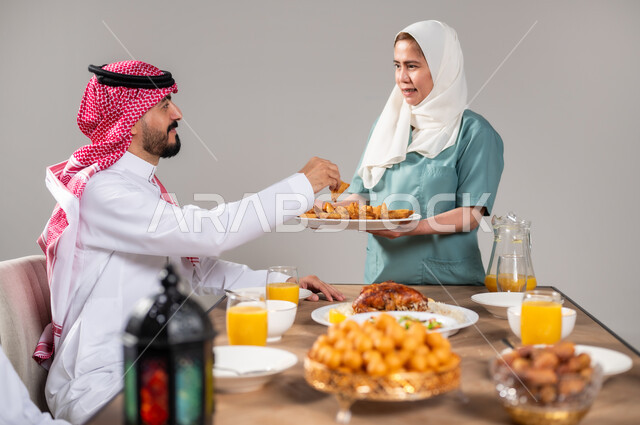 أجواء وعبادات دينية إسلامية، فطور رمضاني عائلي, مائدة إفطار مليئة بأصناف المأكولات والحلويات الشهية, أسرة عربية خليجية سعودية تجلس على سفرة الطعام  قبل موعد الإفطار في شهر رمضان المبارك،استقطاب العمال من الخارج، خلفية رمادية