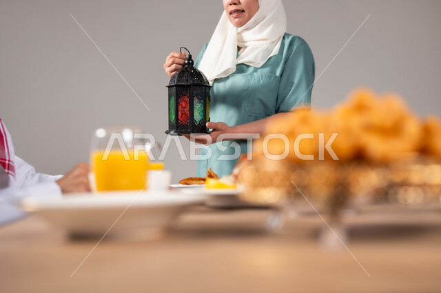 ضيافة رمضانية لذيذة، طبق اللقيمات ذهبية اللون، حلا الزلابيات الشرقي، كرات العجين المقلية الصغيرة، المناسبات والأعياد في المملكة العربية السعودية، تعظيم و تقدير الشهر الفضيل، عاملة منزلية فلبينية تحمل فانوس ملون، خلفية رمادية