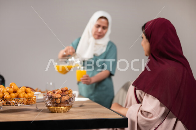 ايماءات السعادة بقدوم الشهر الفضيل,عائلة عربية خليجية سعودية مجتمعة على طاولة الطعام، الاحتفال بالمناسبات و الاعياد الاسلامية, العصائر و الاصناف الشرقية اللذيذة, بورتريه مقرب لعاملة منزلية تقوم بصب العصير و توزيعه, تنظيم سفرة فطور رمضان, خلفية رمادية