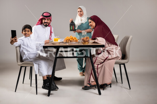 A family Ramadan breakfast, an iftar table full of delicious food items, a Saudi Gulf Arab family sitting on the dining table before iftar time in the holy month of Ramadan, a Filipina worker carrying a colorful lantern, glorifying and appreciating the holy month, gray background