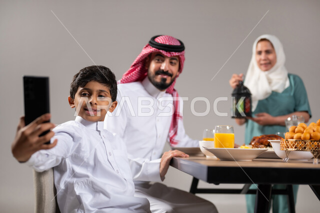 A family Ramadan breakfast, an iftar table full of delicious food items, a Saudi Gulf Arab family sitting on the dining table before iftar time in the holy month of Ramadan, a Filipina worker carrying a colorful lantern, glorifying and appreciating the holy month, gray background